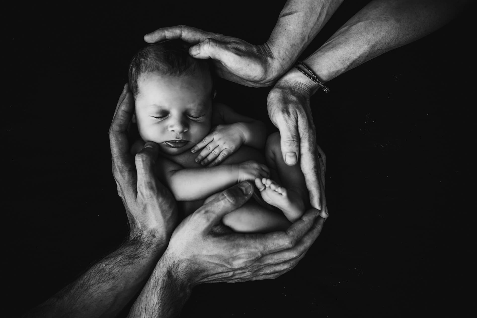 A newborn cradled in the encircling hands of family